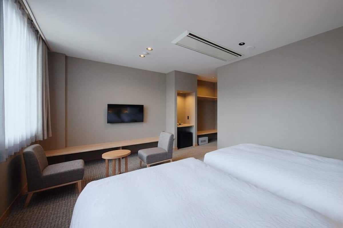 A hotel room with a bed, a desk, a chair, a television, and built-in shelving.