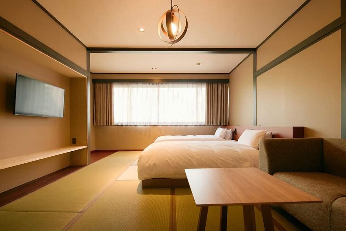 A hotel room with a bed, a sofa, a TV, and a window with curtains.