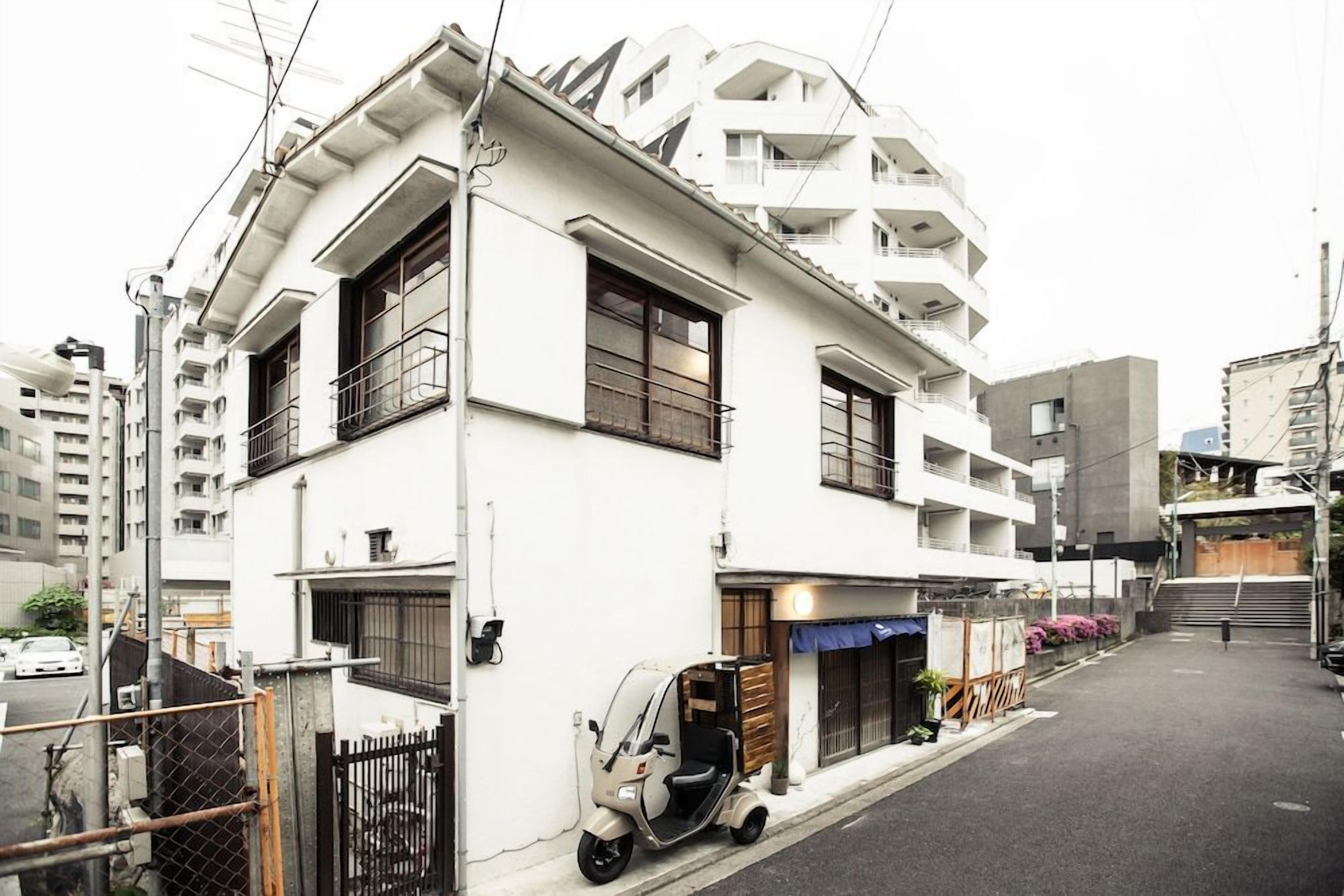 A multi-story residential building with balconies, a parked scooter, and a gated entrance.