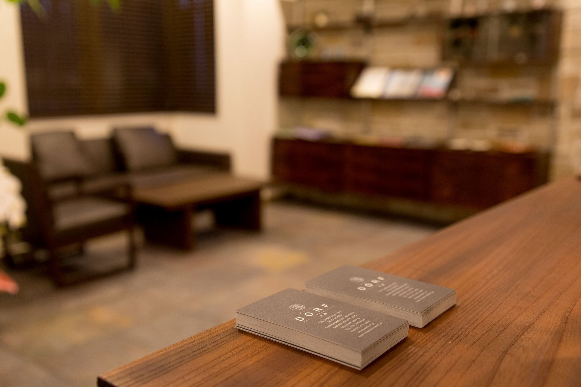 A stack of business cards on a wooden table in a room with a sofa and a bookshelf.