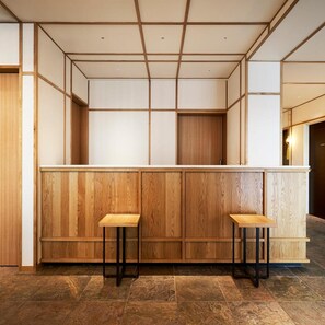 A reception area with a wooden counter, two stools, and a tiled floor. - Tassel Inn Kyoto Kawaramachi Nijo (Kyoto)