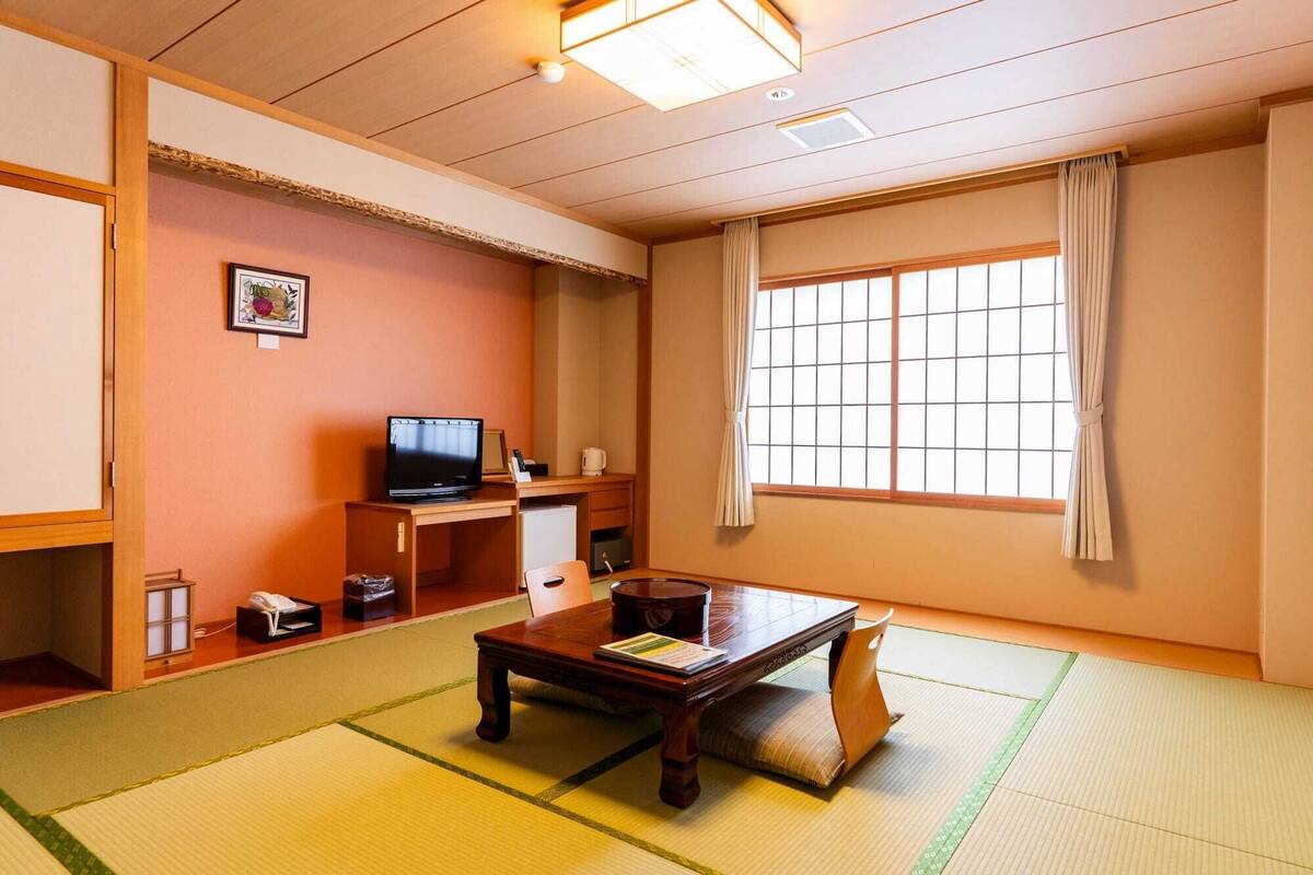 A traditional Japanese-style room with tatami flooring, a television, a small desk, and a window with curtains.