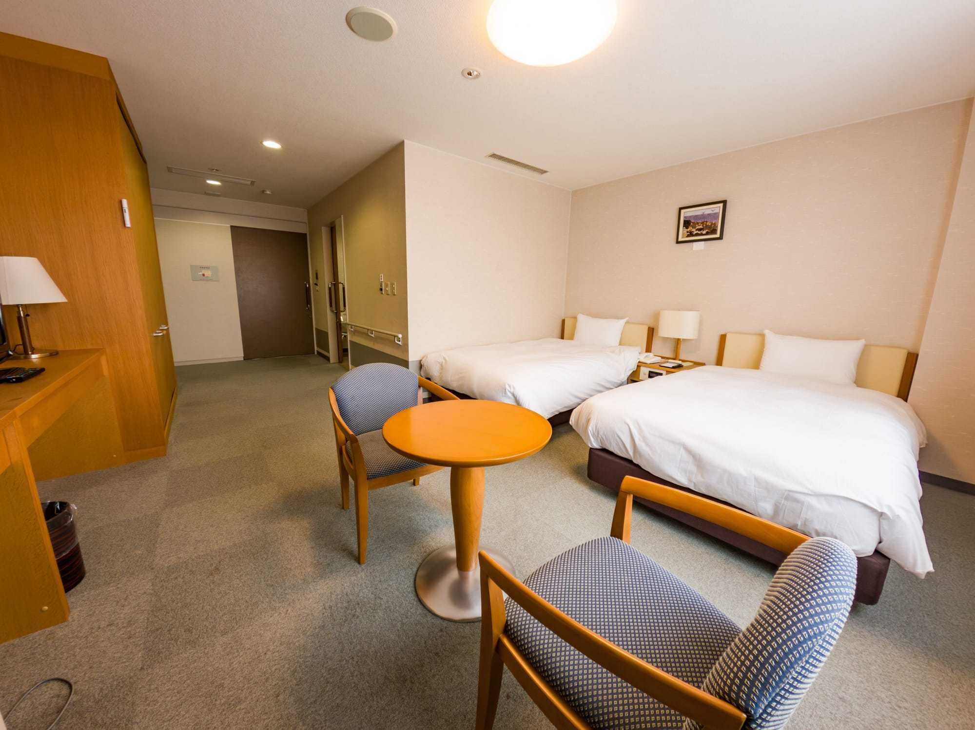 A hotel room with two beds, a desk with a chair, a small round table, and a door leading to another room.