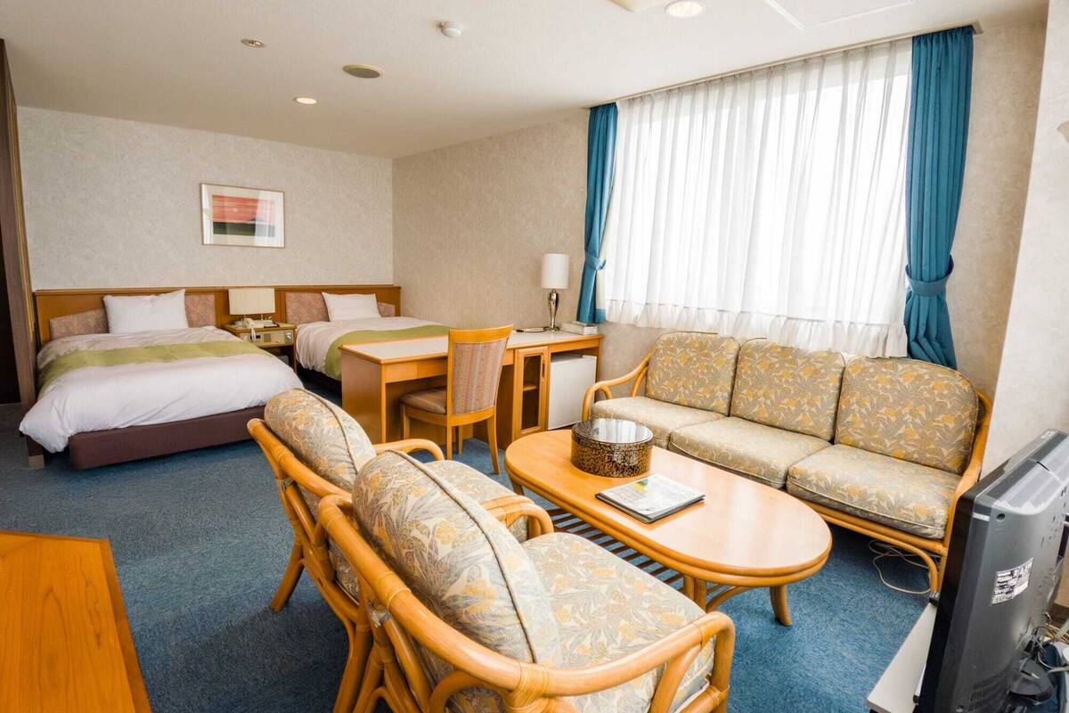 A hotel room with a bed, a sofa, a dining table, and a television.
