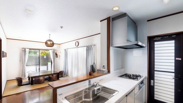 A modern kitchen with a central island, stainless steel appliances, and a large window with curtains. - Sea Stay Okinawa (Onna)