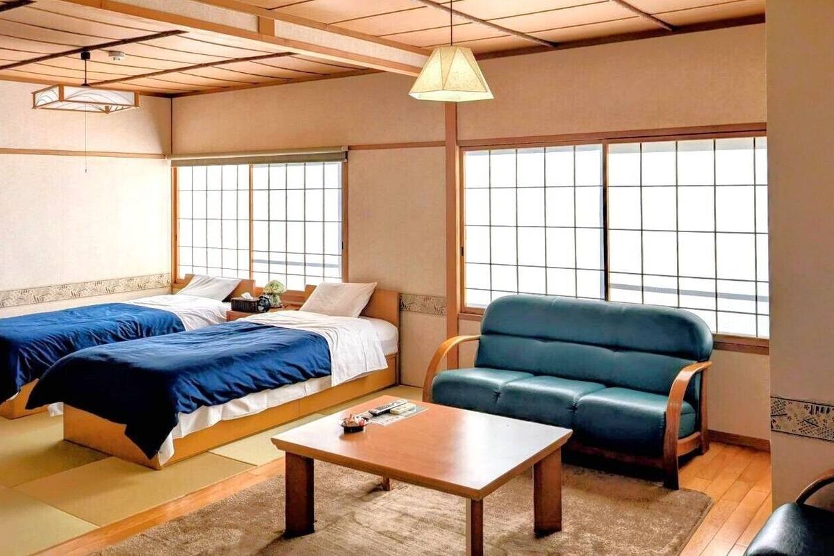 Une pièce de style japonais traditionnel, avec un sol recouvert de tatamis, un lit bas en bois avec une literie bleue, un canapé bleu et une petite table.