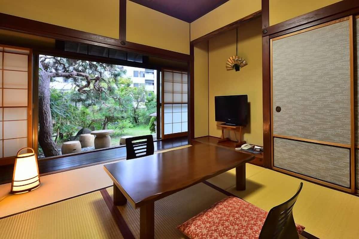 Une pièce de style japonais traditionnel, avec un sol recouvert de tatamis, une table basse, un téléviseur et une porte coulissante.