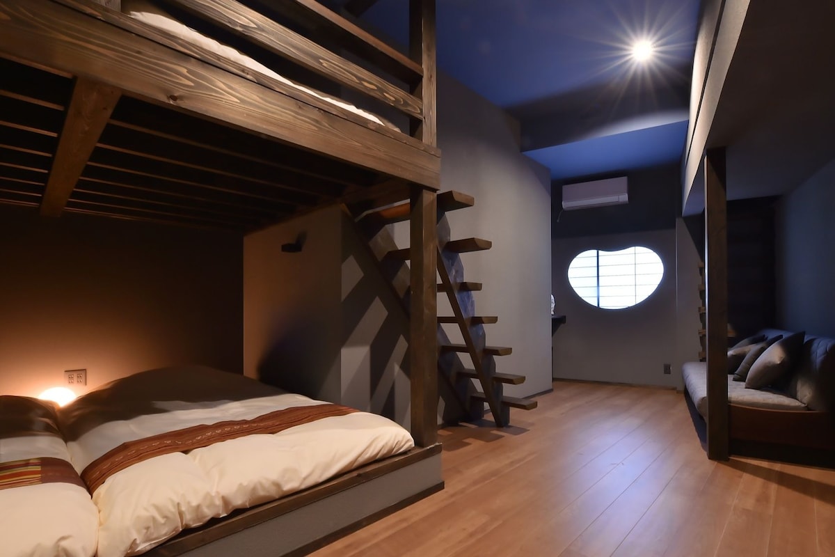 Un dormitorio con una cama litera, una escalera, un ventanal circular y suelo de madera.