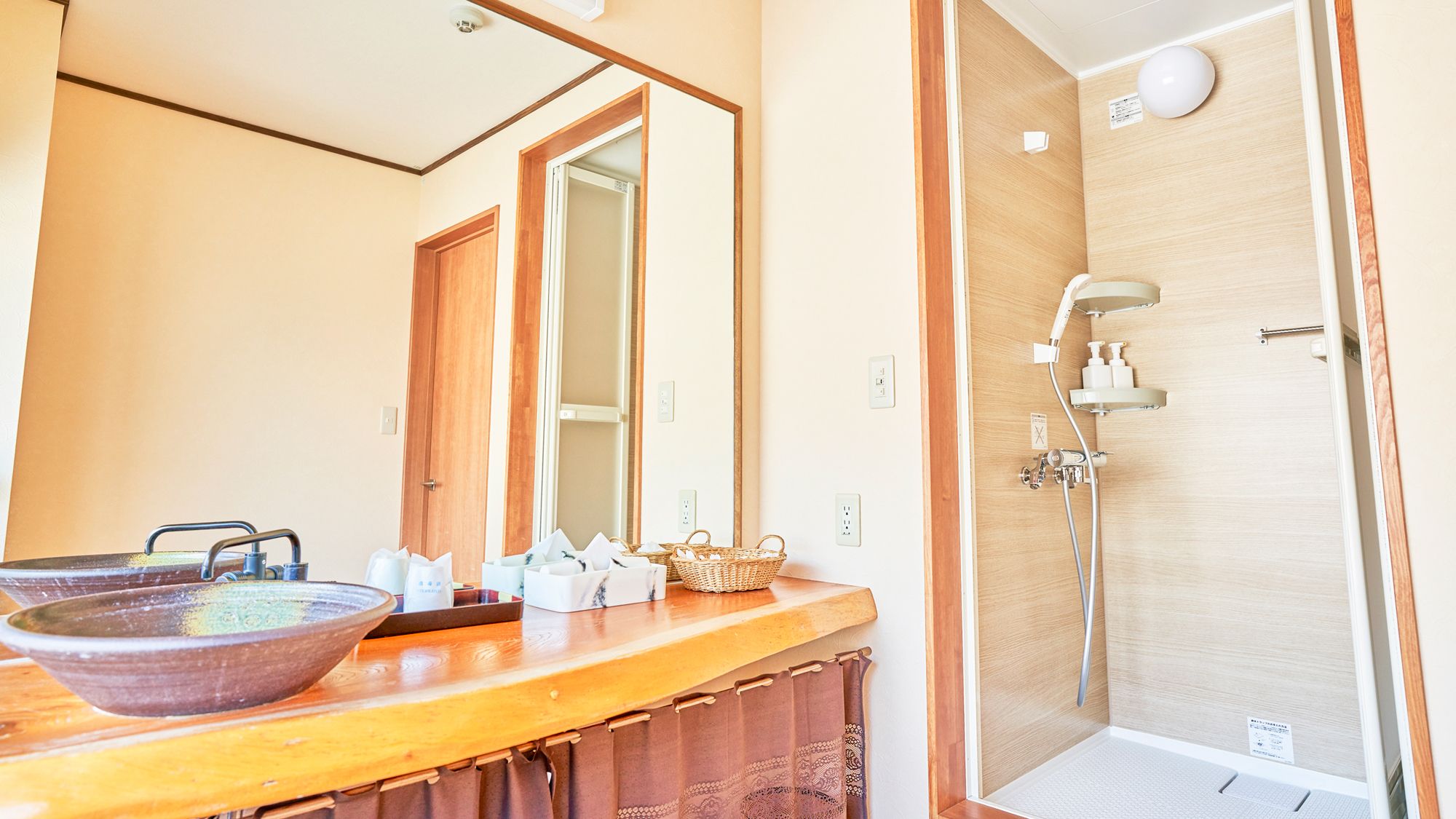 A bathroom with a wooden vanity, a large mirror, a bowl sink, and a shower with a handheld showerhead.