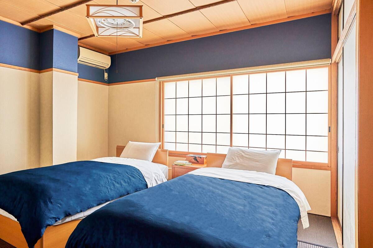 Une chambre d’hôtel avec deux lits, une grande fenêtre et un ventilateur de plafond.