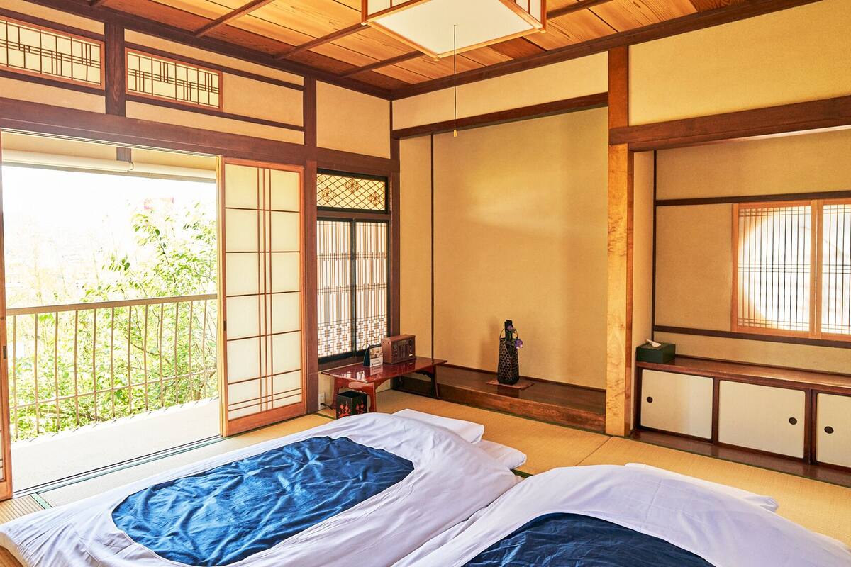 Une pièce de style japonais traditionnel, avec un sol recouvert de tatamis, des portes coulissantes et un lit avec une literie bleue et blanche.