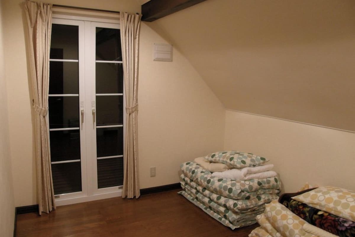Quarto com porta de vidro deslizante, cama com colcha de bolinhas e piso de madeira.