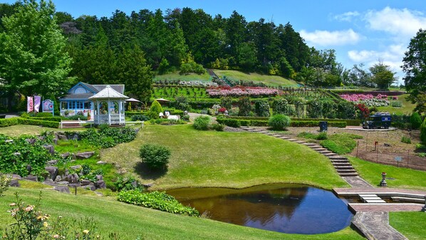 A garden with a pond, a gazebo, and a small building with a blue roof.