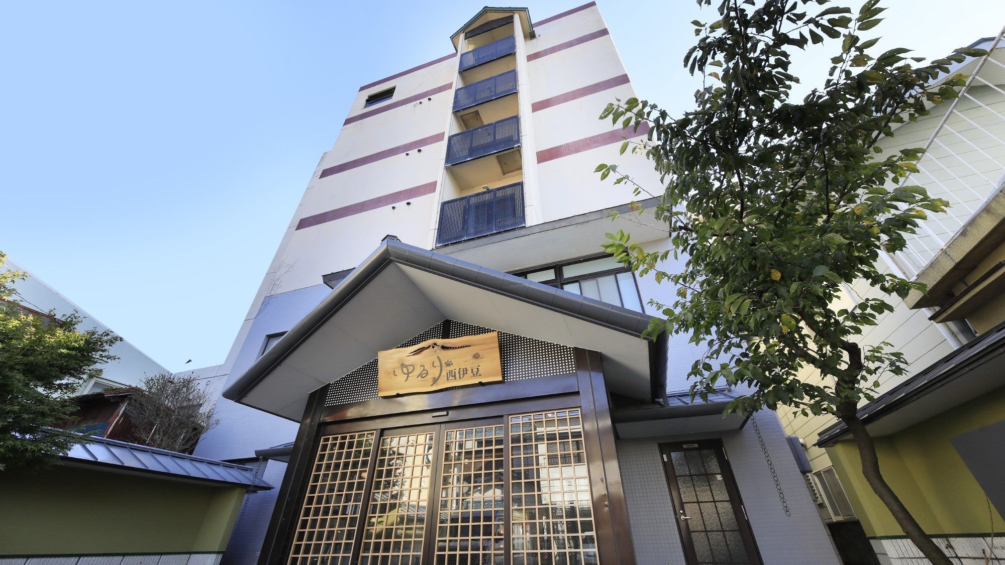 A multi-story building with a traditional Japanese entrance featuring a wooden sign and a grid-patterned gate.