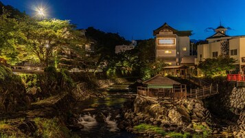 Vista al río con arquitectura tradicional, un puente de madera y un sendero de piedra.