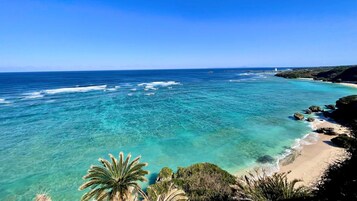 Vista costera con aguas turquesas cristalinas, una playa arenosa y afloramientos rocosos.