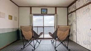 A room with a balcony, two folding chairs, a framed picture on the wall, and a patterned wallpaper on the right wall. - Sea Turtle View Cottage (Wadomari)