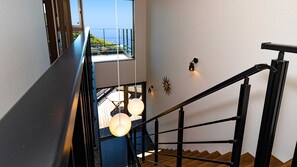Un escalier doté d’une rampe noire et d’une balustrade en verre, menant à un balcon offrant une vue sur la mer.