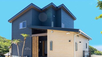 A modern two-story house with a dark blue exterior, a wooden front porch, and a small balcony.