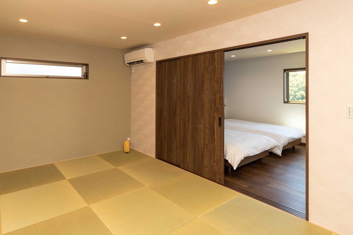 Une chambre à coucher au style minimaliste, dotée d’une grande porte coulissante donnant accès à un espace nuit séparé, d’une petite fenêtre et d’un système de climatisation intégré.