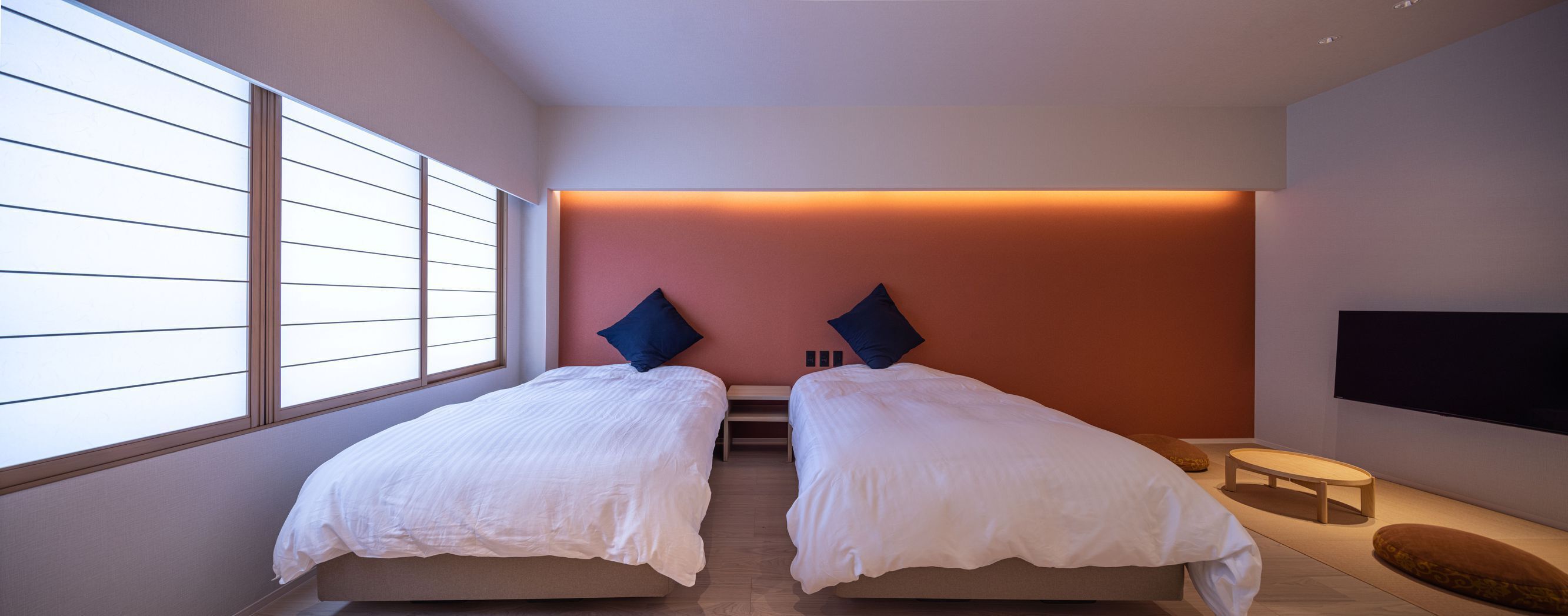 A bedroom with two beds, a TV, and a window with blinds.