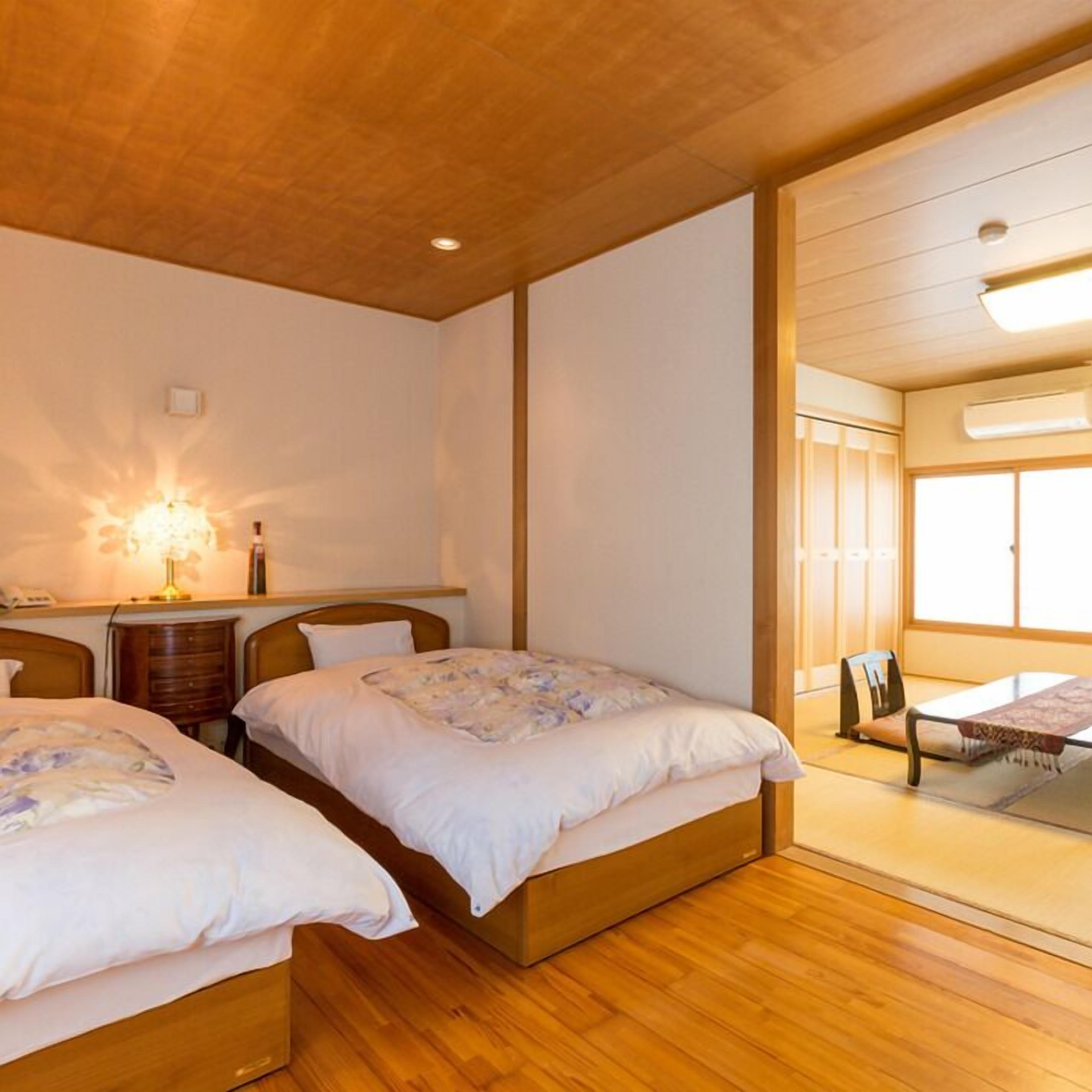 A bedroom with two beds, wooden flooring, a nightstand, a lamp, and a window.