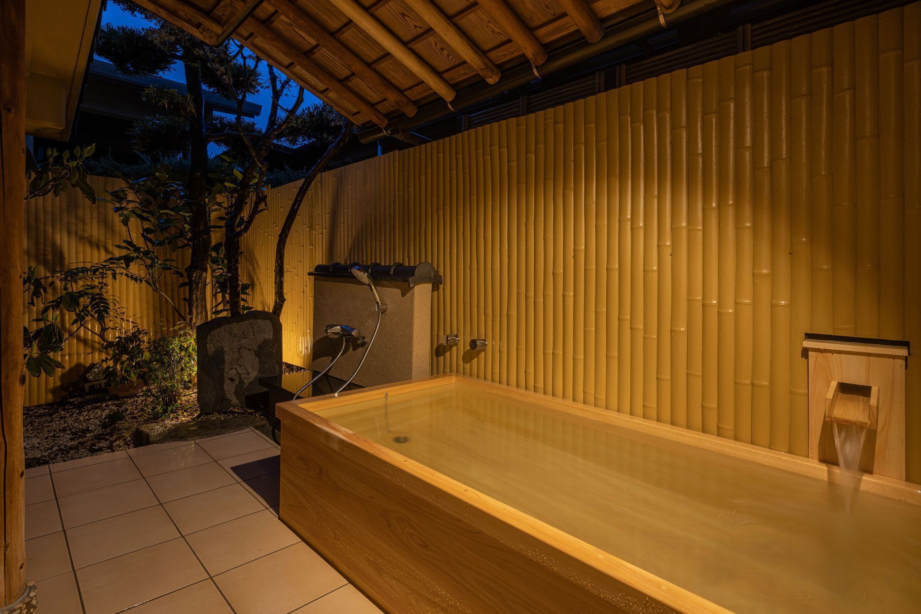 A hot tub in a covered outdoor area with bamboo walls and a tiled floor.