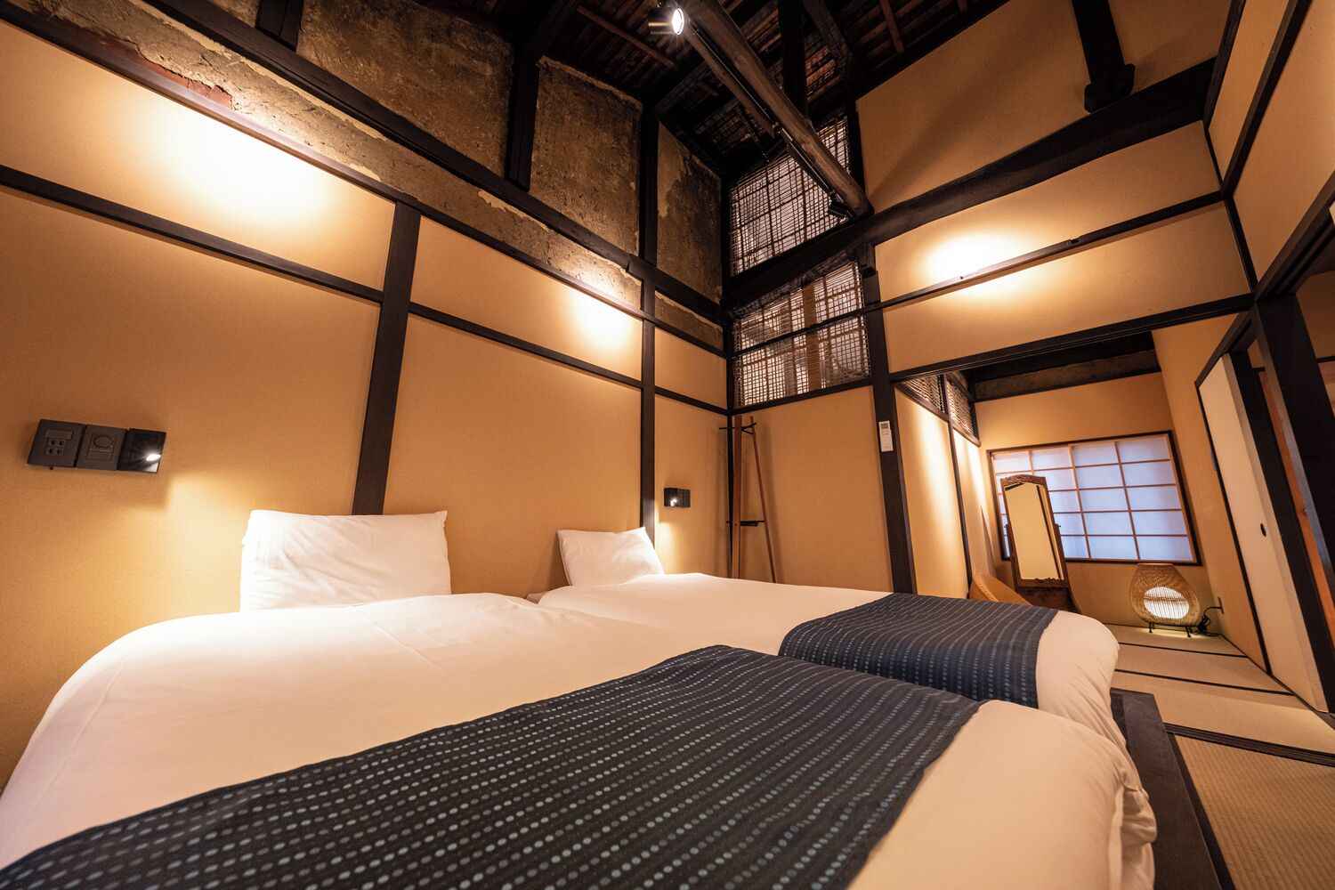 A traditional Japanese-style hotel room with tatami flooring, a large bed with white bedding, a small table, and a shoji screen.