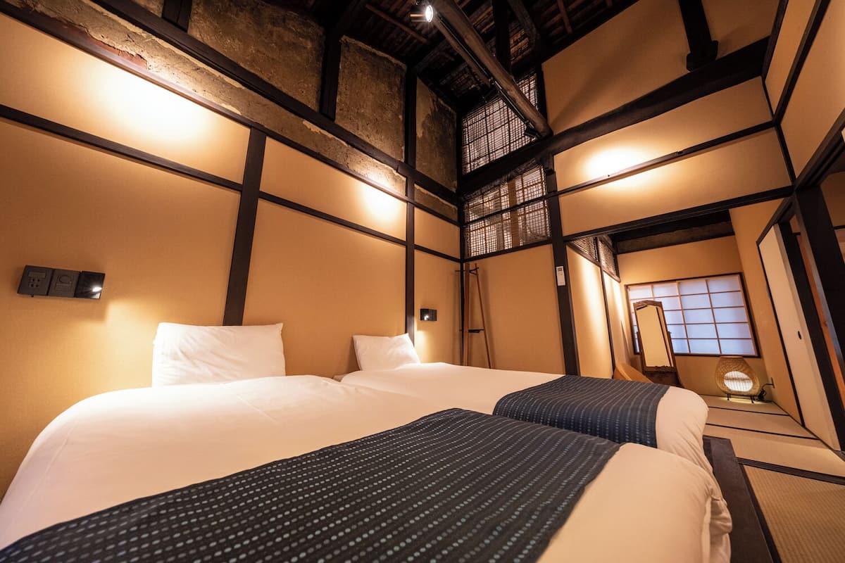 Ein traditionell eingerichtetes japanisches Hotelzimmer mit Tatami-Böden, einem großen Bett mit weißer Bettwäsche, einem kleinen Tisch und einem Shoji-Bildschirm.