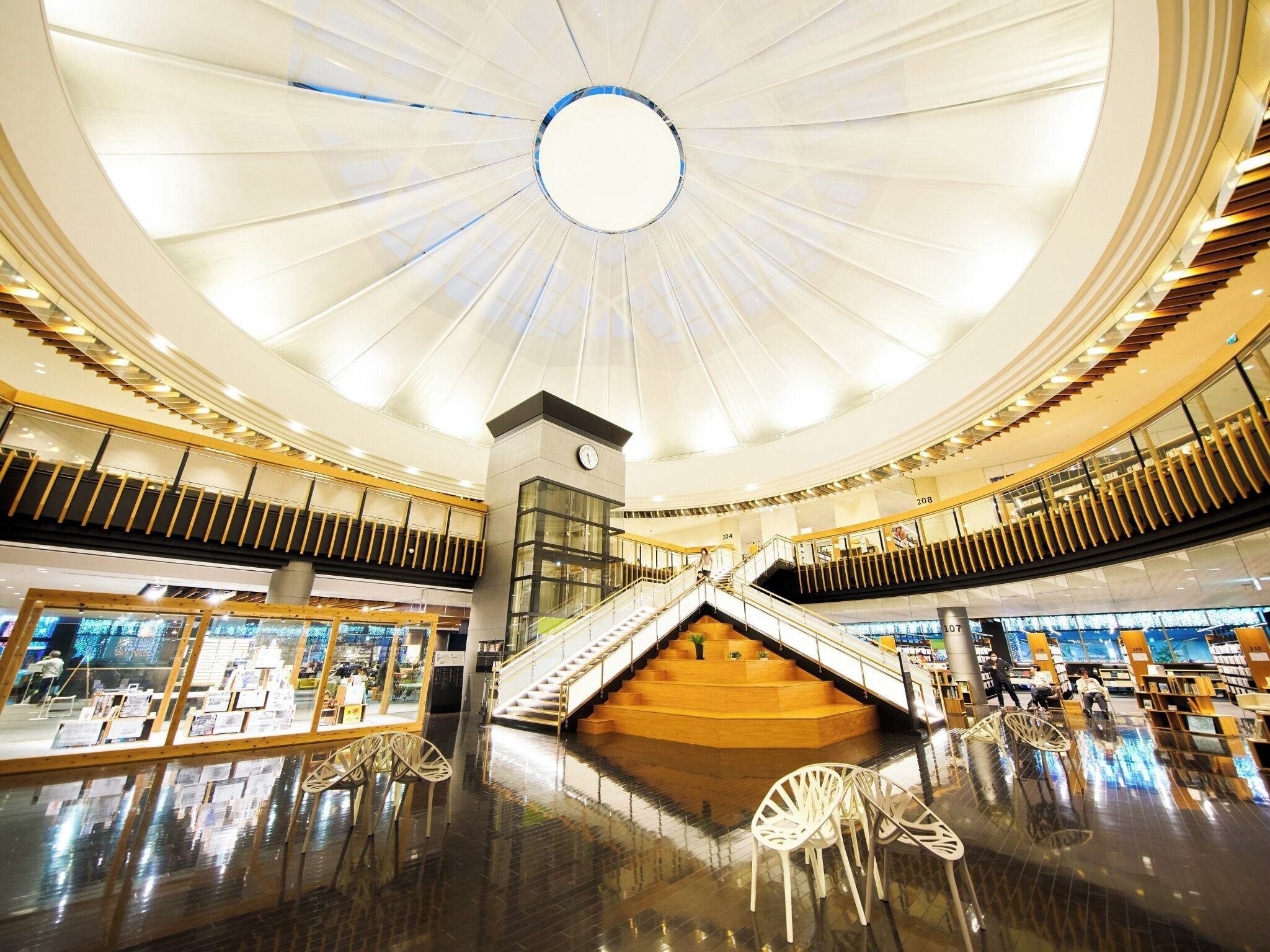 A spacious atrium with a central staircase, glass railings, and a modern ceiling design.