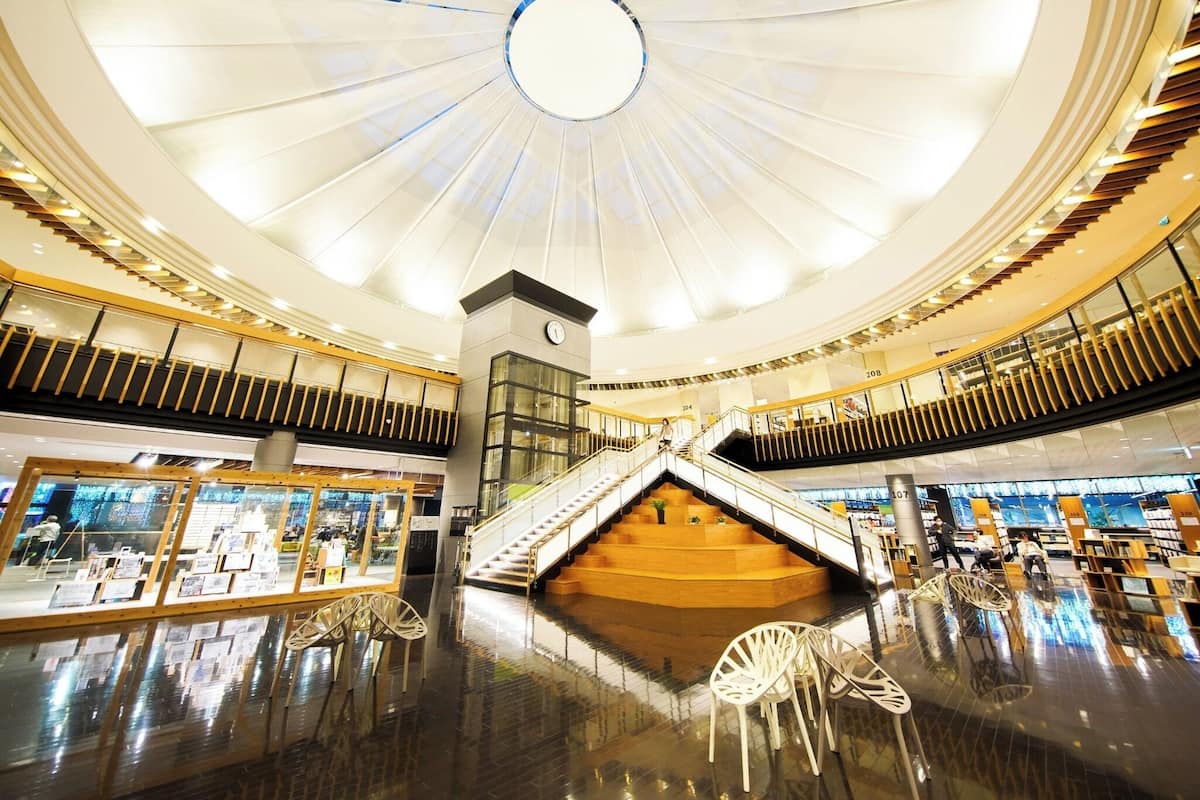 Un amplio atrio con una escalera central, barandillas de cristal y un diseño de techo moderno.