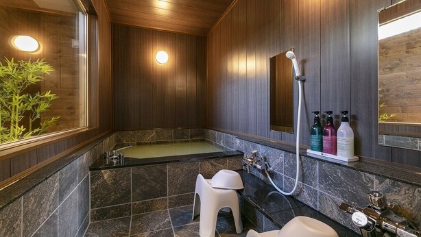 A modern bathroom with a wooden panel wall, a freestanding bathtub, a sink, and a toilet. There are two round lights on the wall and a small plant on the left.