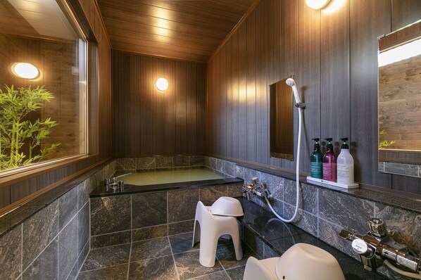 A modern bathroom with a wooden panel wall, a freestanding bathtub, a sink, and a toilet. There are two round lights on the wall and a small plant on the left. - Sakura Jozankei Zen (Sapporo)