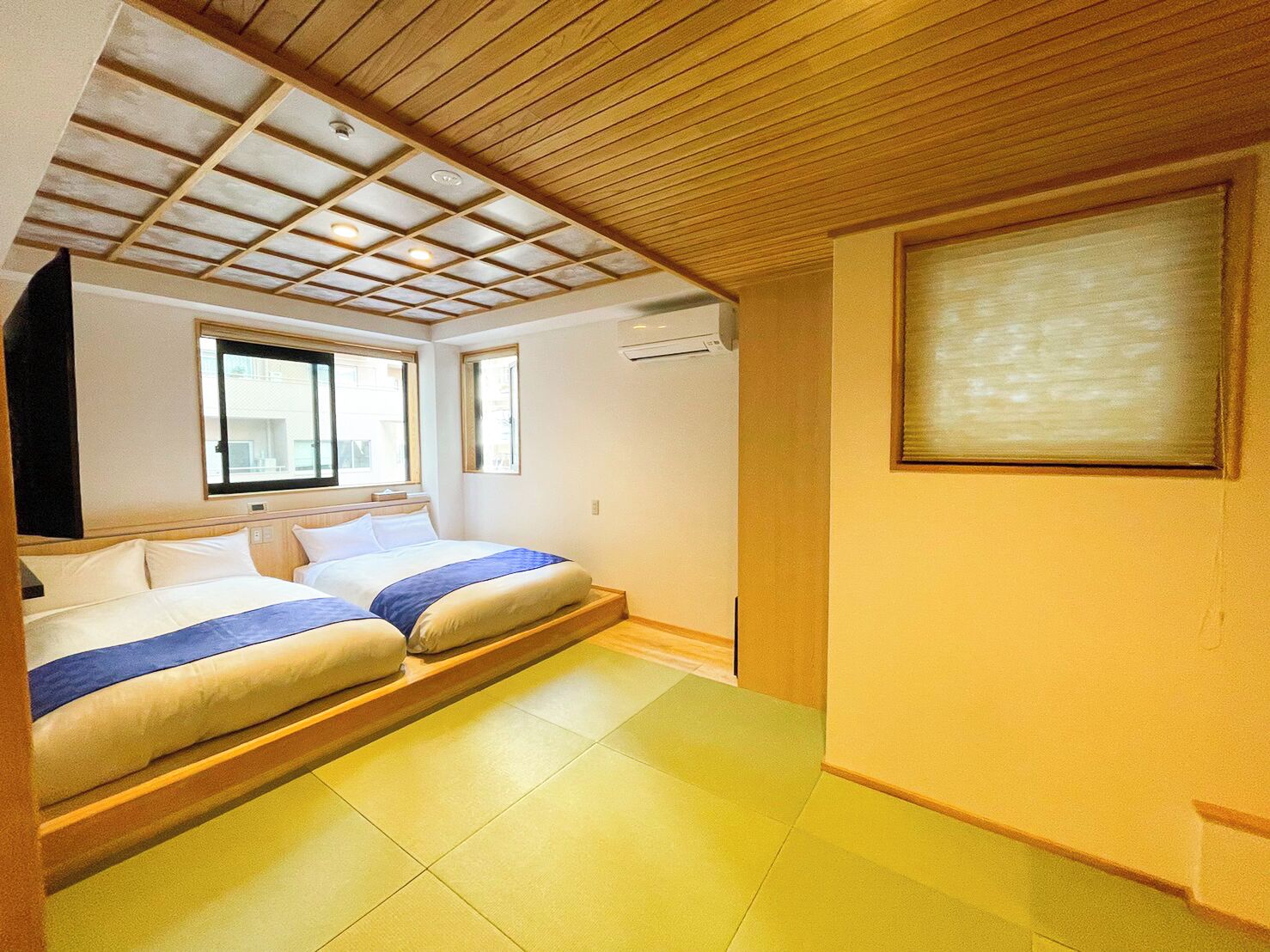 A hotel room with a bed, a window, a wall-mounted air conditioner, and a framed picture.
