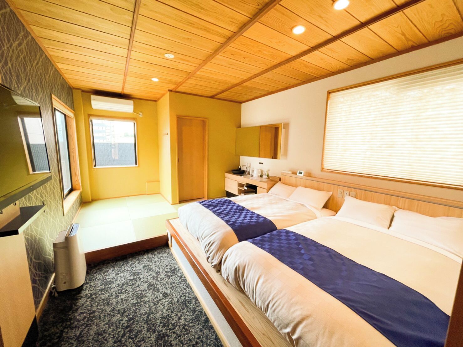 A hotel room with a wooden ceiling, a bed with two pillows, a bedside table, a window, and a mirror.