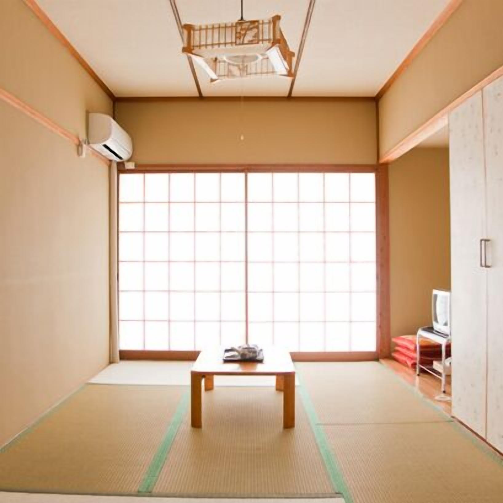 A traditional Japanese room with tatami flooring, a sliding door, a small table, and a television.
