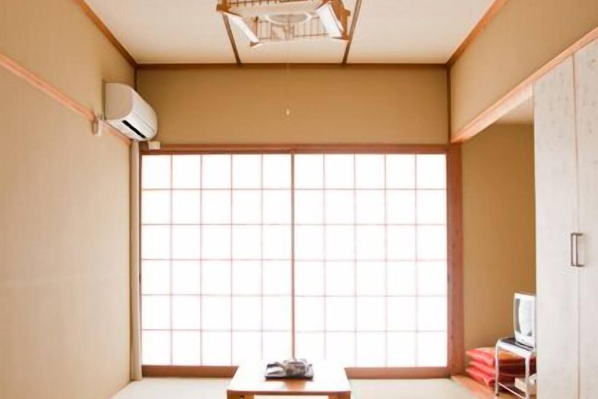 A traditional Japanese room with tatami flooring, a sliding door, a small table, and a television.