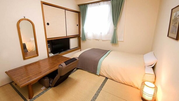 Ein Hotelzimmer mit Bett, Schreibtisch mit Stuhl, Fernseher, Fenster mit Vorhängen und einer Nachttischlampe.