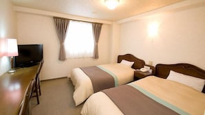 Ein Hotelzimmer mit zwei Betten, einem Schreibtisch mit Fernseher und einem Fenster mit Vorhängen.