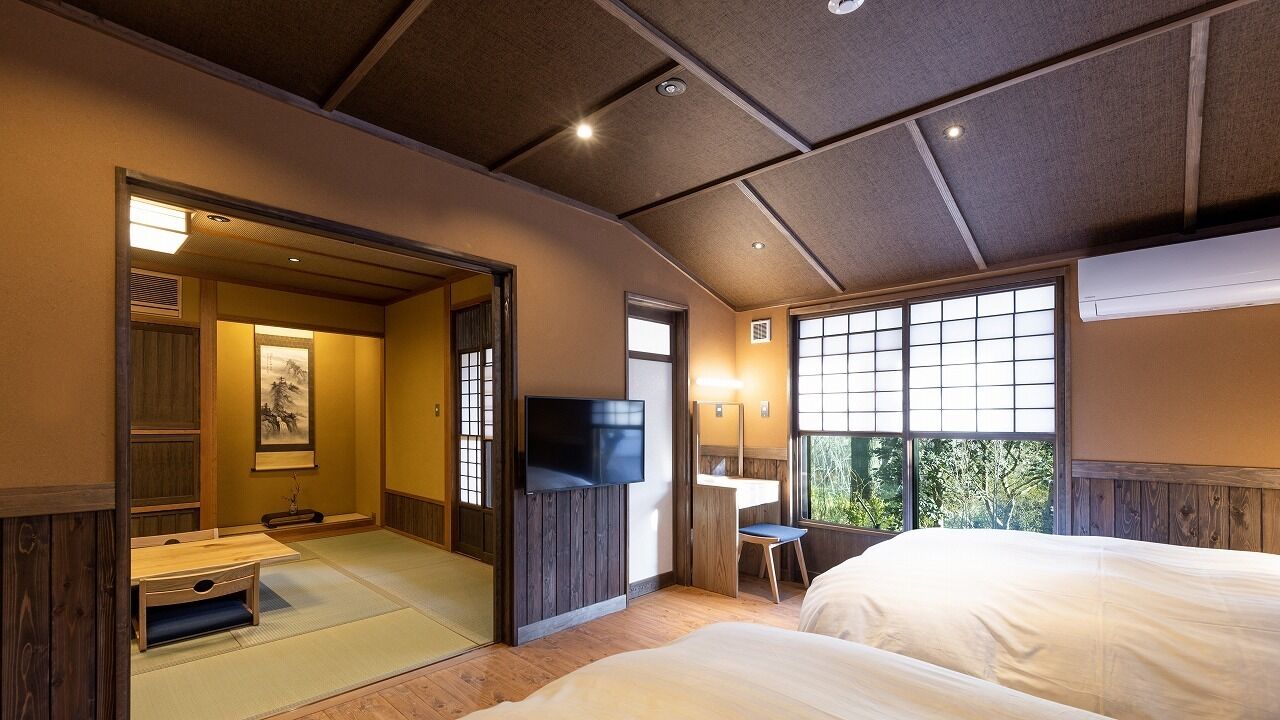 A traditional Japanese-style room with tatami flooring, a television, a desk, and a large window.