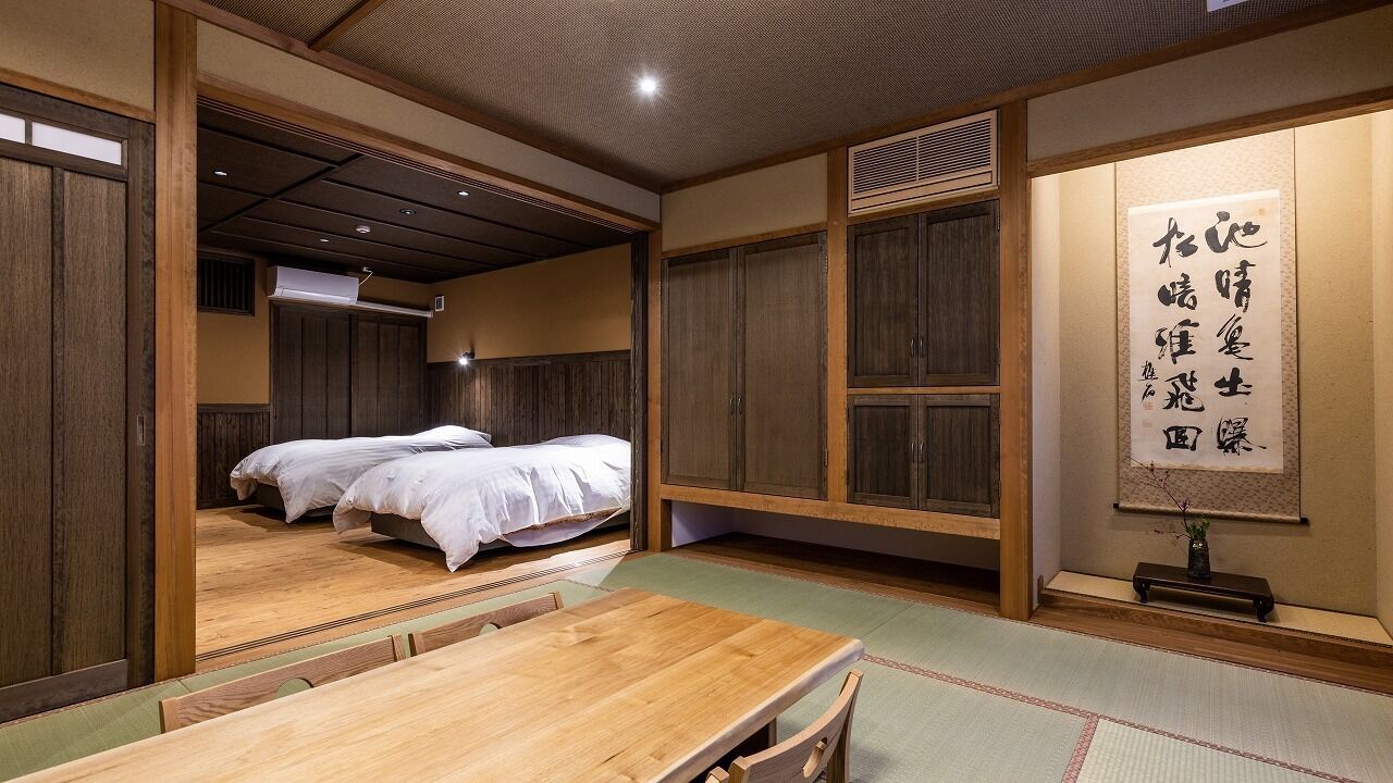 A traditional Japanese room with tatami flooring, a wooden table, two beds, and a shoji screen.