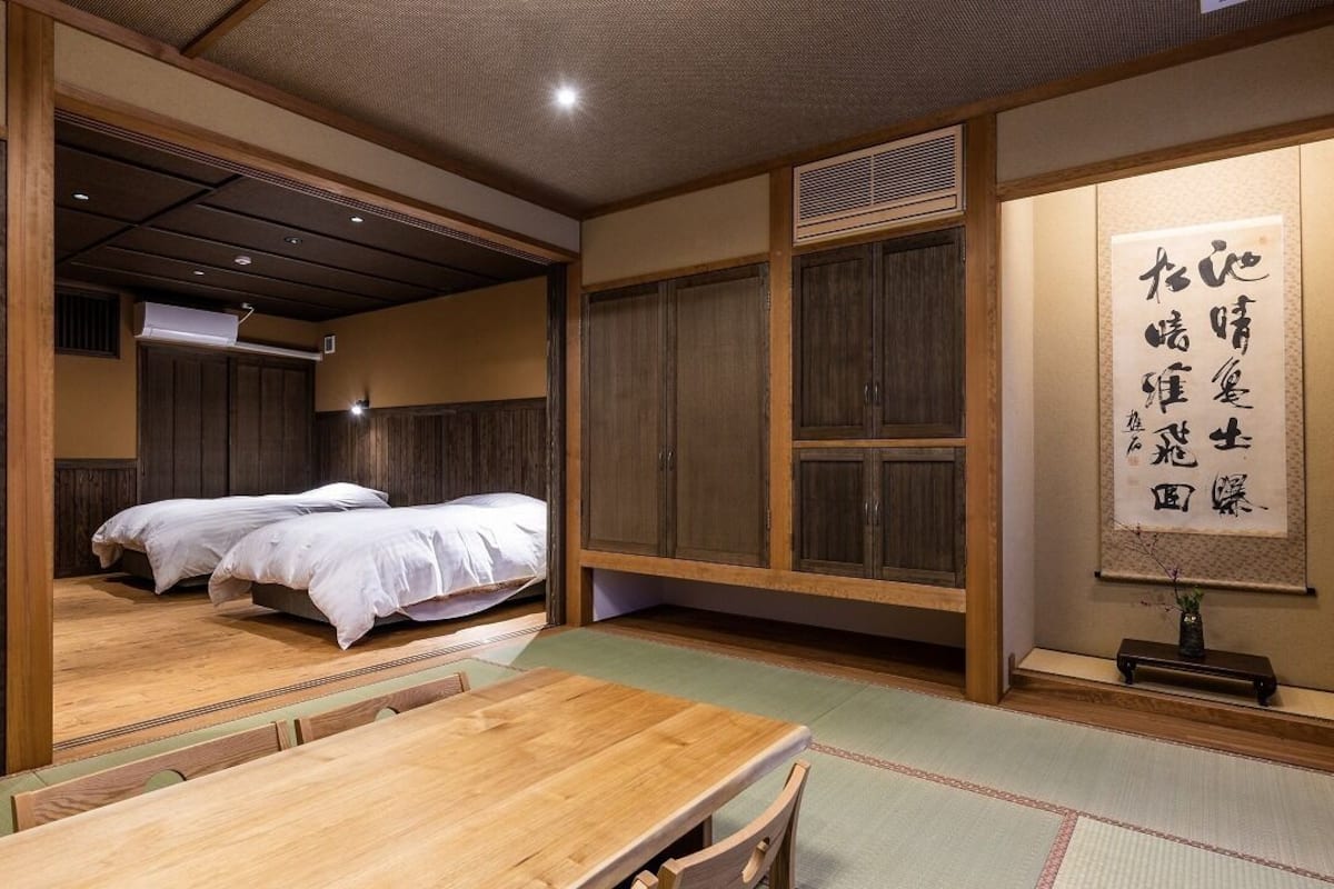 Una habitación japonesa tradicional con suelo de tatami, una mesa de madera, dos camas y un panel de fusuma.