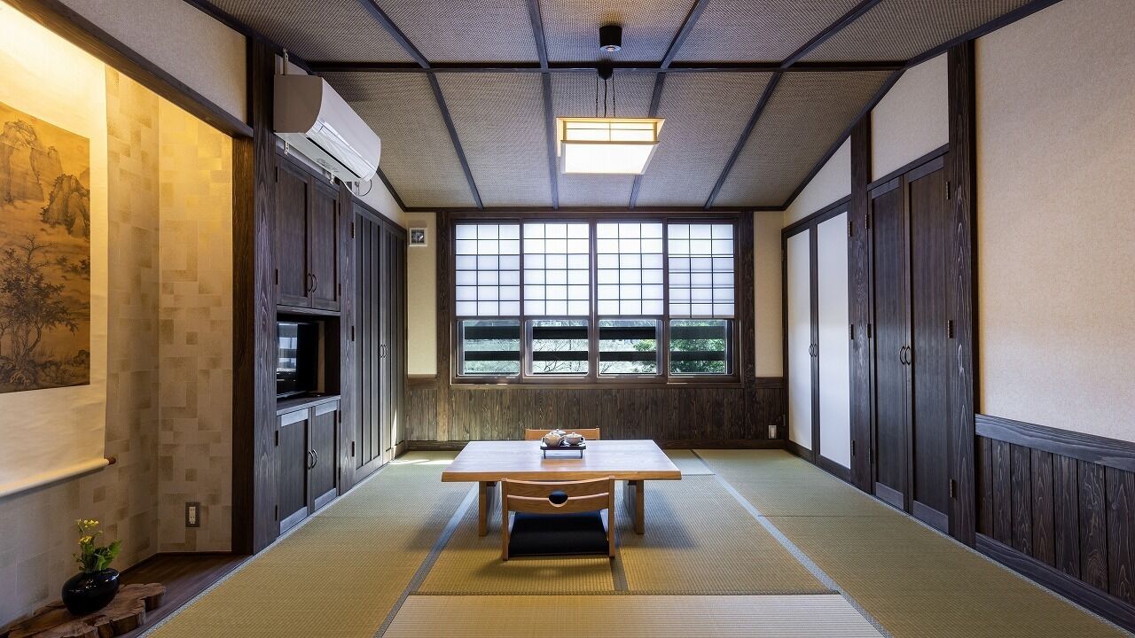 A traditional Japanese room with tatami flooring, a low table, sliding doors, and a large window.