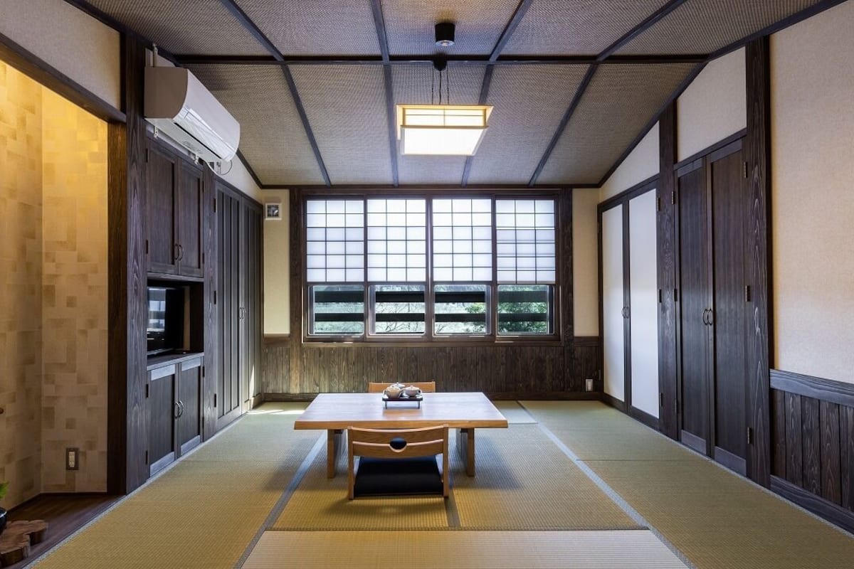 Una habitación japonesa tradicional con suelo de tatami, una mesa baja, puertas correderas y un ventanal grande.