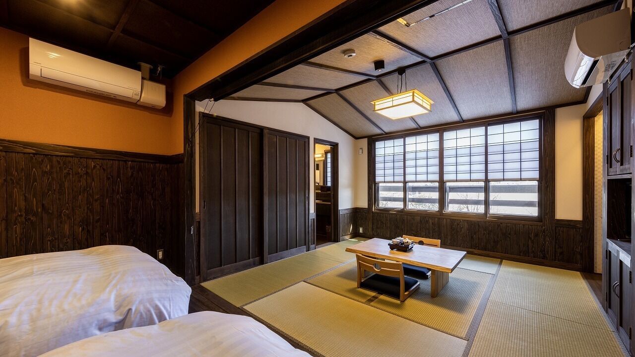 A traditional Japanese room with tatami flooring, a low table, and two beds.