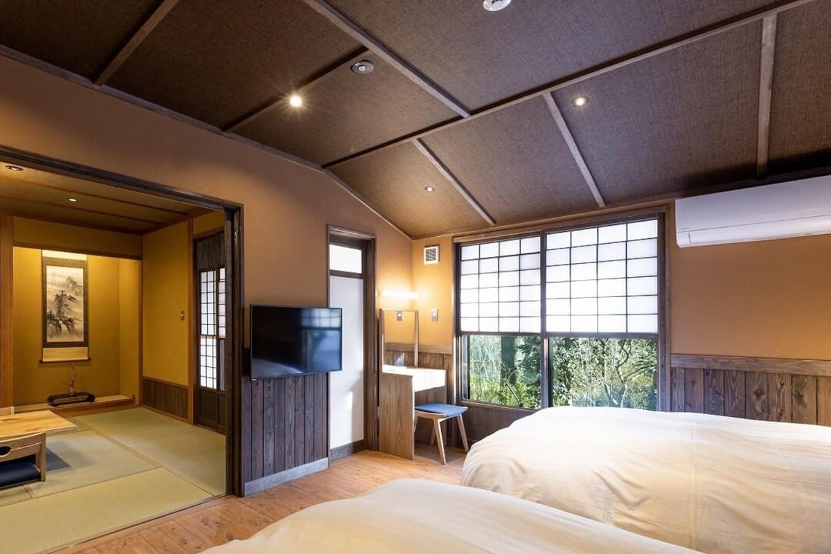 Una habitación japonesa tradicional con suelo de tatami, televisión, escritorio y un ventanal grande.