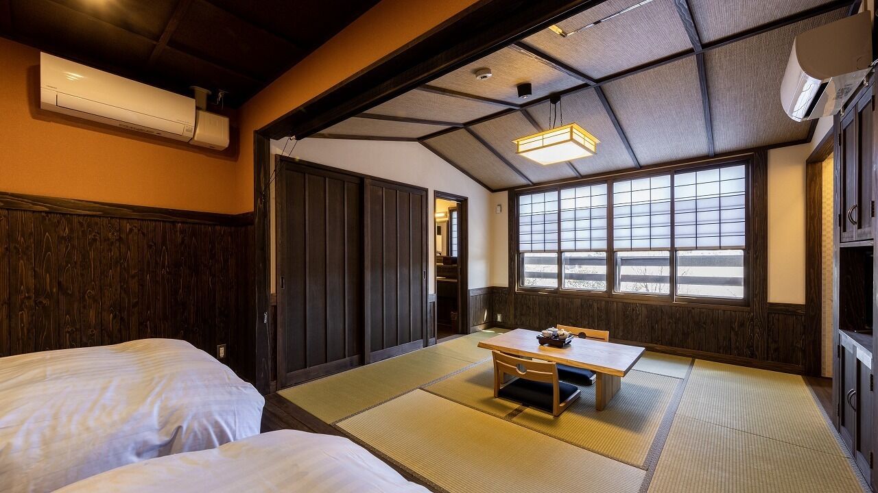 A room with two beds, a table, and a view through large windows.