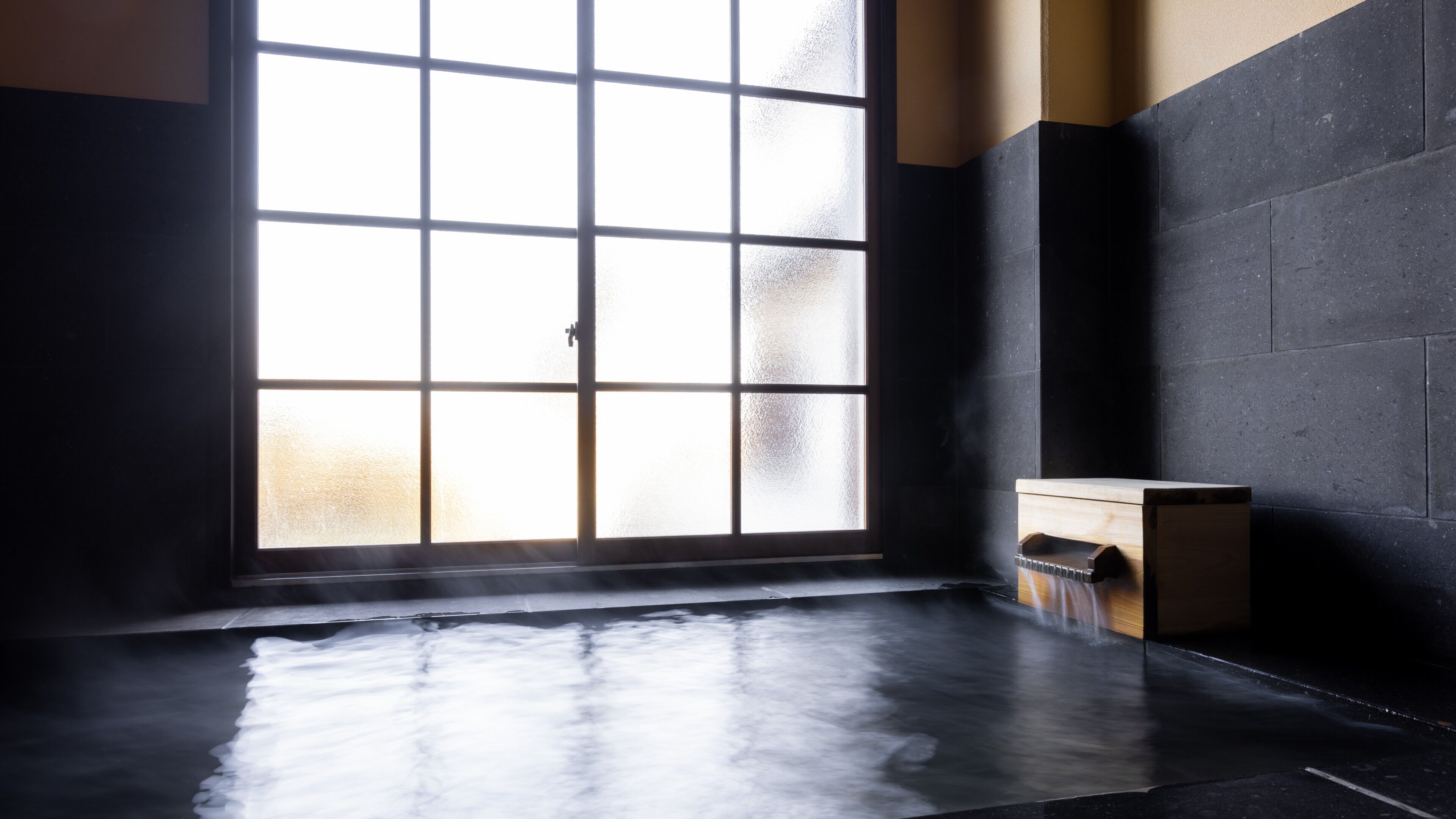 A room with a large frosted window, a wooden bench, and a tiled floor.