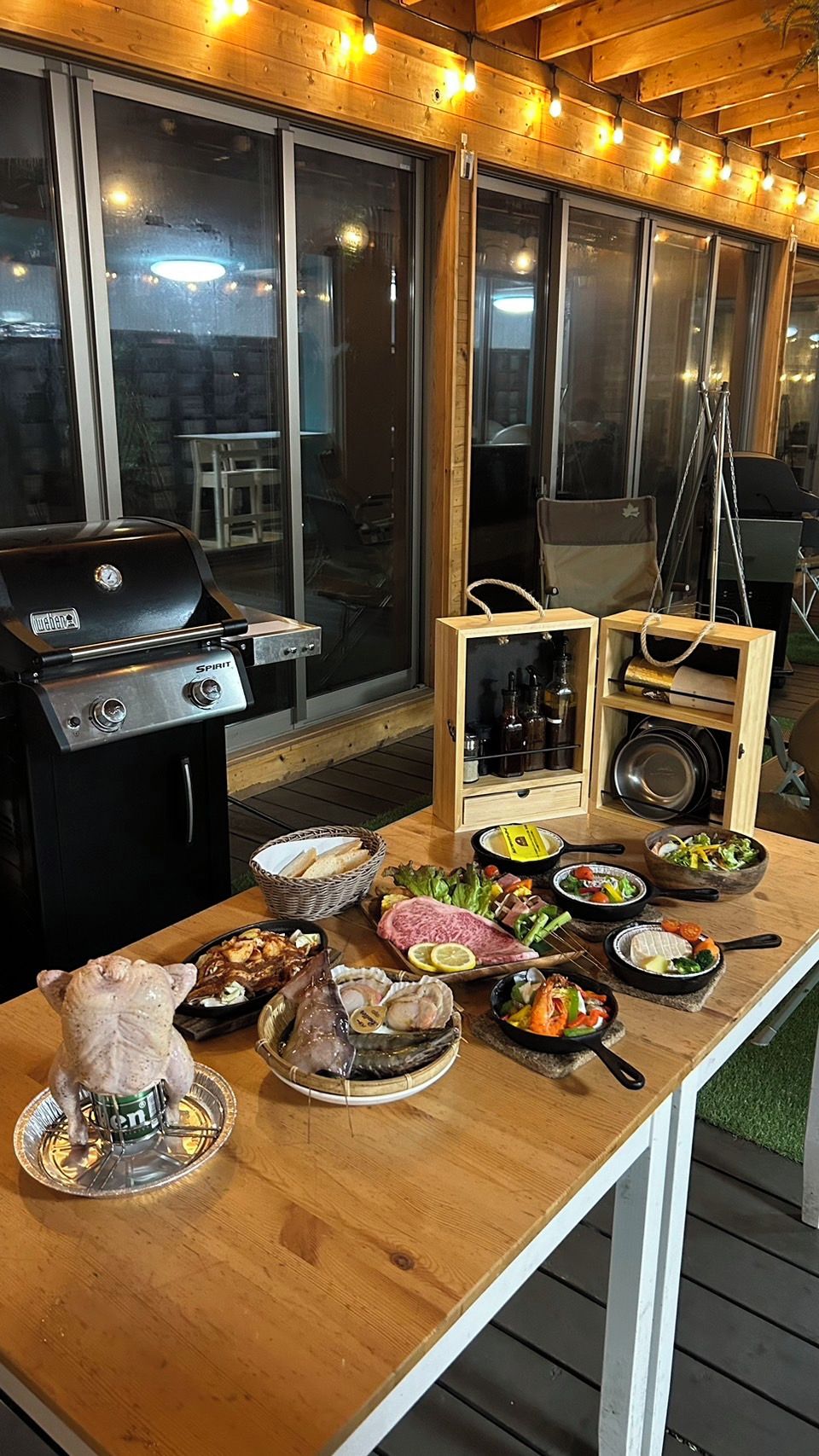 Un área de comedor al aire libre con una parrilla, mesas de madera y diversos alimentos.