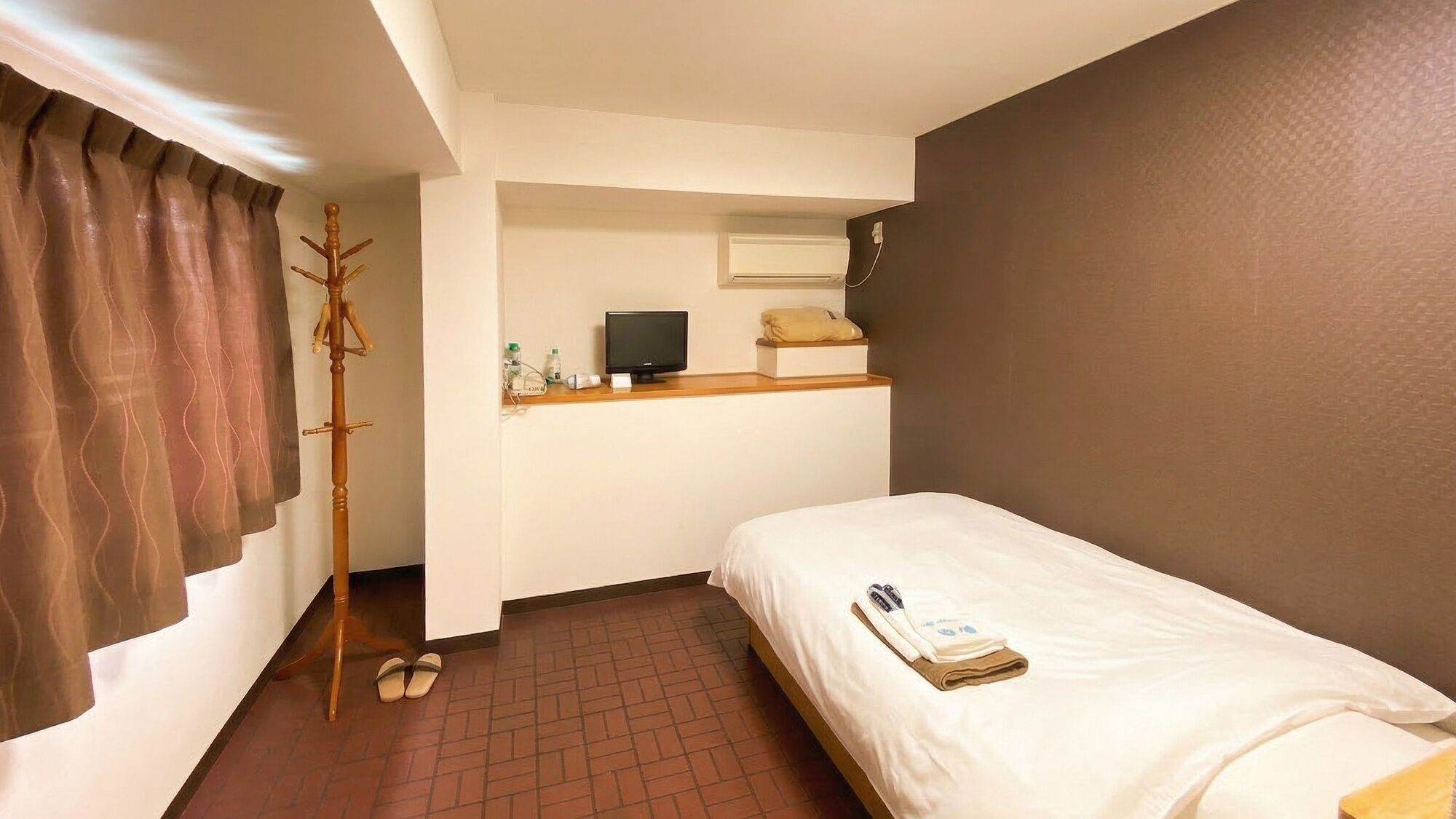 Kompakti hotellihuone, jossa on yksi sänky, televisio, naulakko ja pieni hylly, jossa on hygieniatarvikkeita.